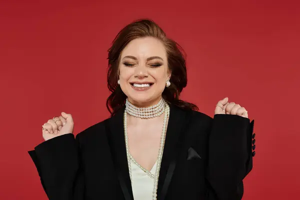A joyful young woman in elegant attire stands out against a vivid red background. — Stock Photo
