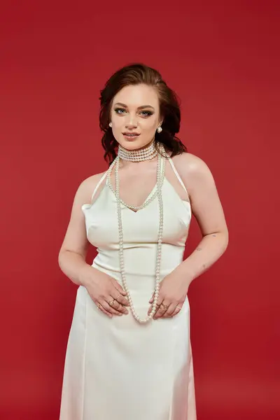 A young beautiful woman in a stunning outfit showcases elegance with a striking red background. — Stock Photo