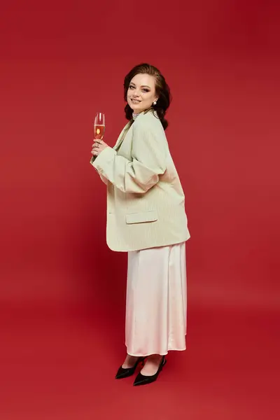 Dressed in stylish clothing, a young woman joyfully toasts with a glass, radiating elegance. — Stock Photo