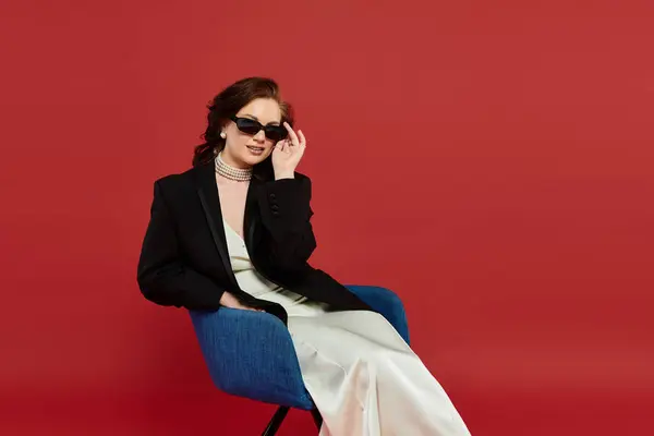 A young, beautiful woman lounges elegantly in stylish attire against a striking red background. — Stockfoto