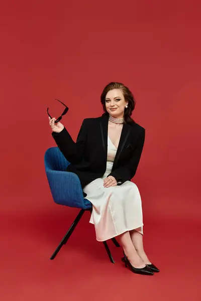 The elegant woman sits confidently, showcasing her stylish outfit against a bold backdrop. — Stock Photo