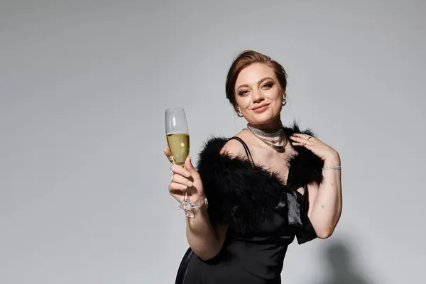 Une jeune femme dans une élégante robe noire lève un verre de champagne tout en célébrant joyeusement. — Photo de stock