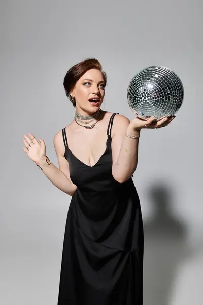 A young woman dressed in elegant attire expertly holds and poses with a shimmering disco ball. — Stock Photo