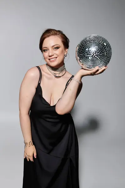 A joyful woman in a sleek black outfit showcases a dazzling disco ball. — Stock Photo