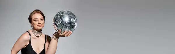 A stylish young woman in an elegant outfit confidently holds a shimmering disco ball. — Stock Photo