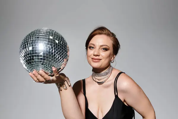 A beautiful young woman, dressed elegantly, playfully holds a sparkling disco ball, exuding charm. — Stock Photo