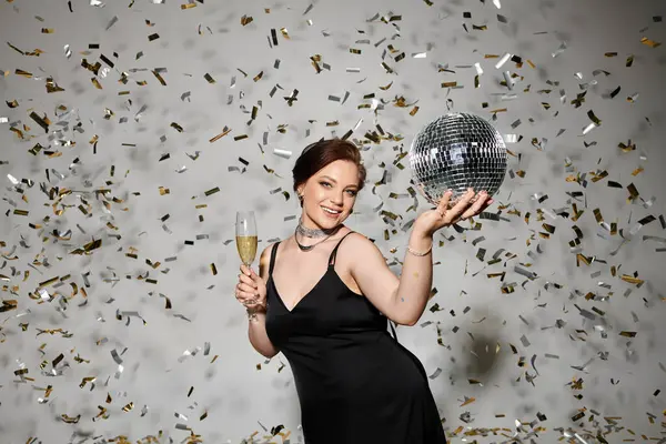 A young woman in an elegant black dress raises a champagne glass amidst sparkling confetti. — Stock Photo