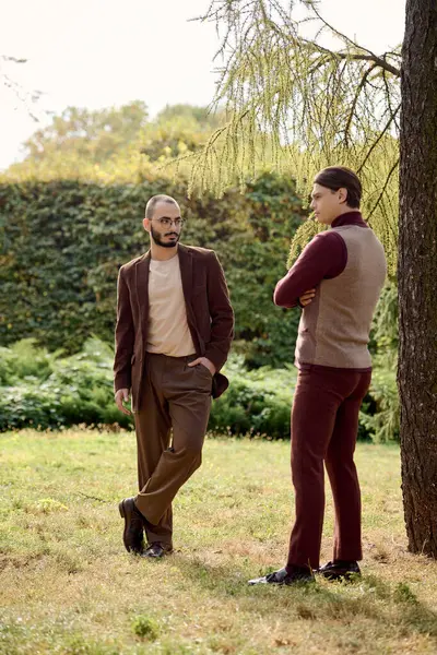 Zwei gut aussehende Männer posieren selbstbewusst in stylischer Herbstkleidung inmitten einer ruhigen Naturlandschaft. — Stockfoto