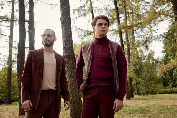 Two fashionable men pose confidently in a beautiful autumnal field surrounded by vibrant trees. — Stock Photo