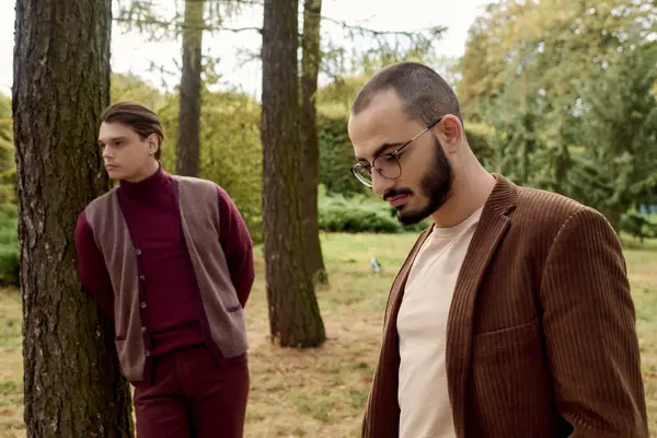 Two stylish men pose amidst trees, showcasing autumn fashion against the backdrop of colorful foliage. — Stock Photo