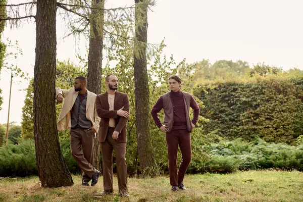 Tres caballeros de moda muestran sus estilos otoñales mientras disfrutan de la serena belleza de la naturaleza. - foto de stock