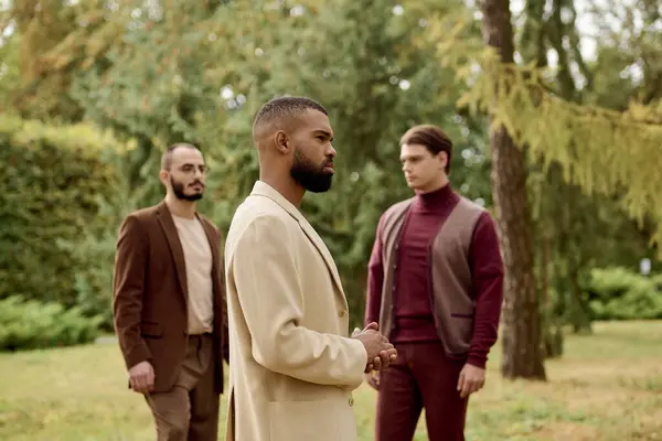 Three handsome men dressed in fashionable autumn outfits pose gracefully in a peaceful outdoor setting. — Stock Photo