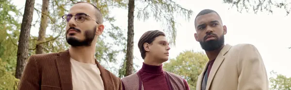 Three handsome men showcase their autumn fashion while surrounded by vibrant fall foliage in a tranquil field. — Stock Photo