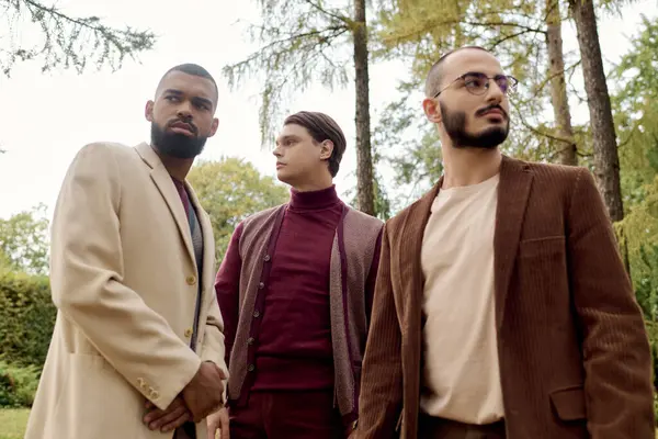 Handsomeness radiates as three men showcase their stylish autumn attire amidst vibrant, falling leaves. — Stock Photo