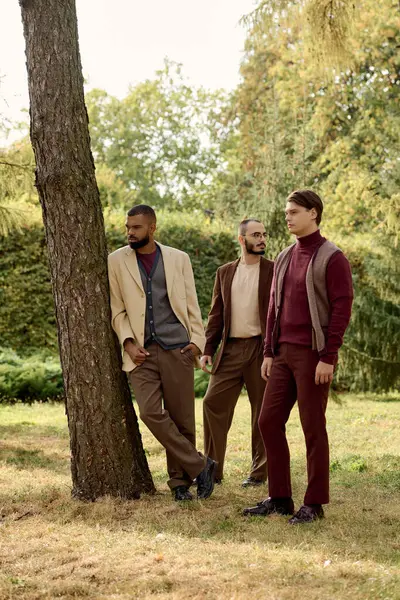Three handsome men showcase fashionable autumn outfits while relaxing in a tranquil field of golden foliage. — Stock Photo