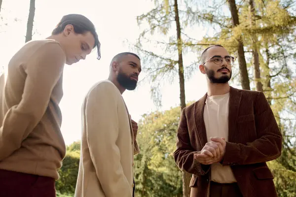 Three handsome men showcase autumn fashion while posing in a beautiful field surrounded by trees. — Stock Photo