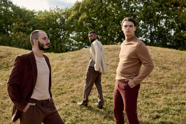 Three men in fashionable autumn attire stand in a tranquil field, embodying seasonal style and charm. — Stock Photo