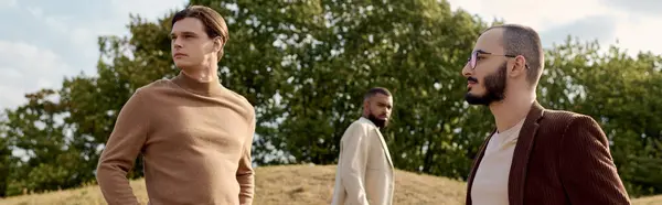 Three handsome men display their fashionable autumn outfits while enjoying the tranquility of a sunny field. — Stock Photo