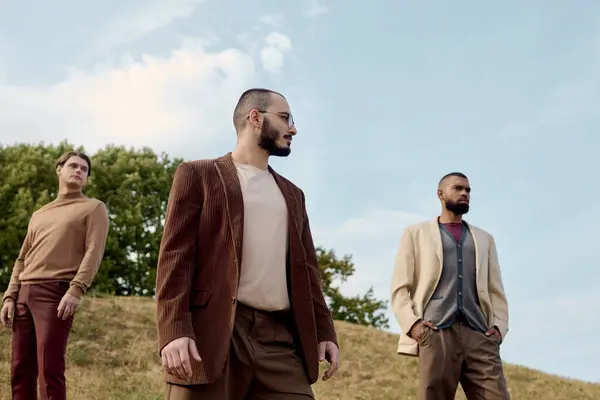 Three handsome men dressed in autumn attire pose confidently in a tranquil natural setting. — Stock Photo