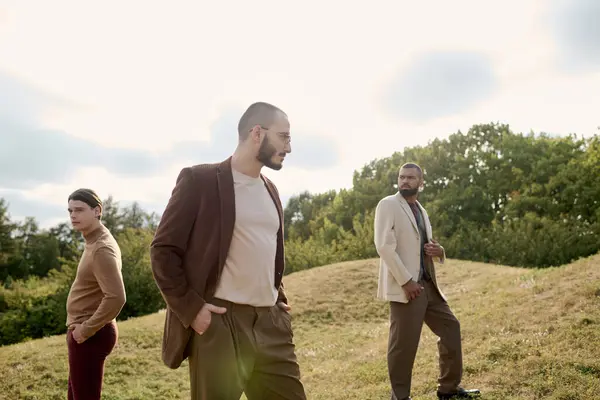 Three stylishly dressed men pose confidently in an autumn field under soft, warm sunlight. — Stock Photo