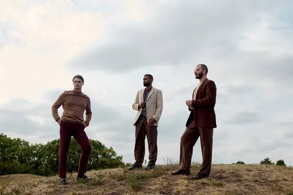 Three handsome men showcase autumn fashion while posing confidently amidst a serene, colorful field. — Stock Photo