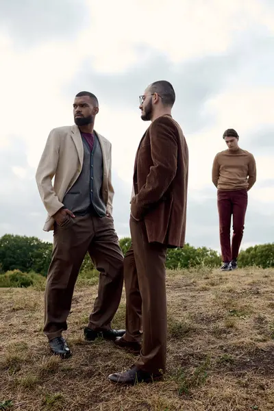 Três homens na moda ficam confiantes em um campo de outono, mostrando suas roupas elegantes contra a natureza.. — Fotografia de Stock