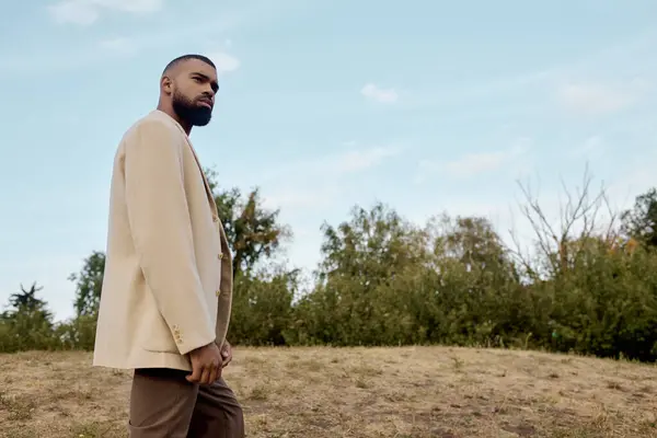 Vestido con ropa de otoño de moda, un hombre camina con gracia a través de un paisaje tranquilo rodeado de naturaleza. - foto de stock