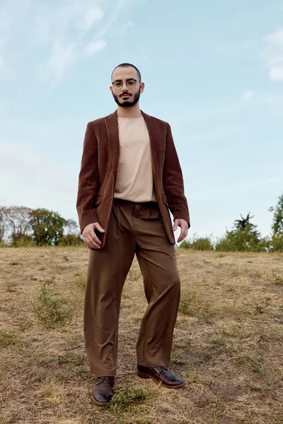 A handsome man poses confidently in a field, dressed in stylish autumn fashion amidst vibrant nature. — Stock Photo
