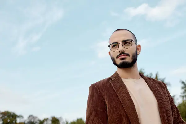 A handsome man dressed in autumn attire stands confidently in a serene natural setting, enjoying the day. — Stock Photo
