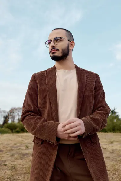 Ein modischer Mann steht selbstbewusst auf einem Feld und umarmt die pulsierende Herbststimmung mit Wärme. — Stockfoto