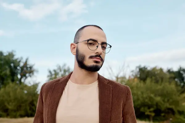 A fashionable man stands confidently in a sunlit field, showcasing autumn style amidst nature's beauty. — Stock Photo