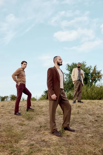 Três homens confiantes posar em roupas de outono elegantes contra um cenário natural sereno, celebrando o estilo. — Fotografia de Stock