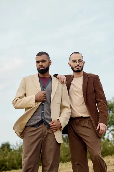Two handsome men dressed in fashionable autumn attire pose confidently in a picturesque natural setting. — Stock Photo