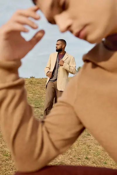Handsome men display fashionable autumn outfits against a serene natural backdrop, embodying seasonal elegance. — Stock Photo