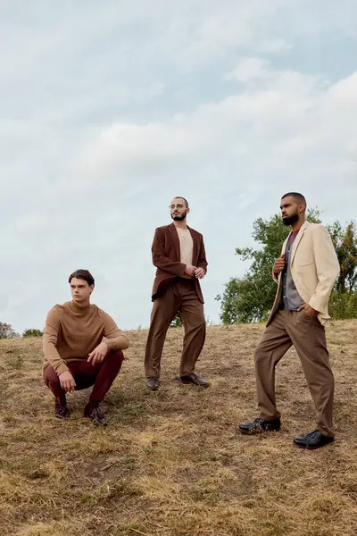Three handsome men stand in a serene autumn landscape, dressed in fashionable outfits that blend elegance and nature. — Stock Photo