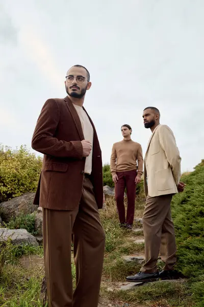 Tres hombres guapos posan con confianza en atuendo de otoño, rodeados de naturaleza vibrante bajo un cielo nublado. — Stock Photo