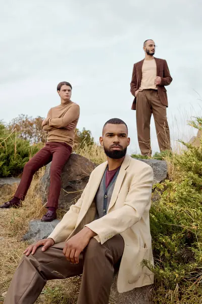 Three handsome men pose in a scenic field, embracing stylish autumn attire amid nature beauty. — Stock Photo