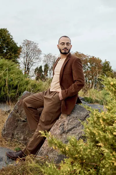 A handsome man showcases stylish autumn fashion while posing gracefully in a tranquil field of nature. — Stock Photo