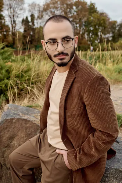 A handsome man in fashionable autumn clothing stands proudly in a tranquil field surrounded by nature. — Stock Photo