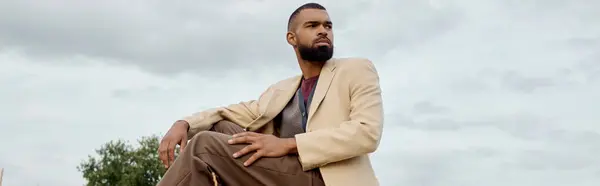 A handsome man showcases autumn fashion while sitting thoughtfully in a peaceful natural setting. — Stock Photo
