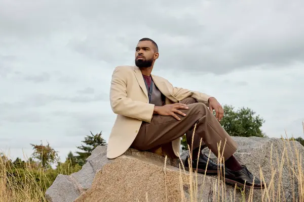 A handsome man dressed in fashionable autumn attire poses thoughtfully in a tranquil field, surrounded by nature. — Stock Photo
