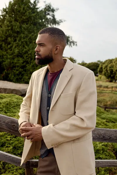 A well-dressed man poses thoughtfully among vibrant autumn foliage in a tranquil outdoor setting. — Stock Photo