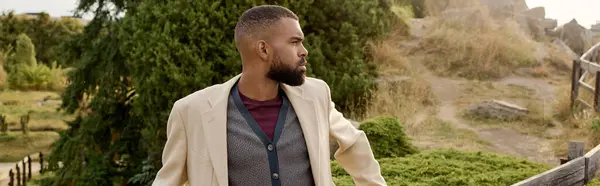 A fashionable man stands confidently in a picturesque autumn landscape surrounded by colorful foliage. — Stock Photo