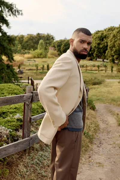 A stylish man poses confidently in a scenic field, surrounded by the warm hues of autumn foliage. — Stock Photo