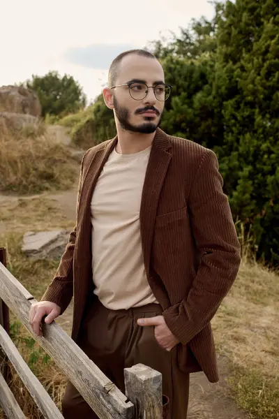 A handsome man dressed in autumn attire stands confidently in a picturesque field surrounded by nature. — Stock Photo