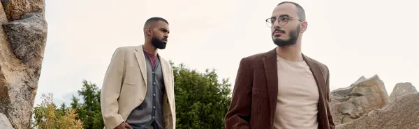 Dois homens bonitos em trajes de outono na moda posar com confiança em um ambiente natural, incorporando estilo sazonal. — Fotografia de Stock