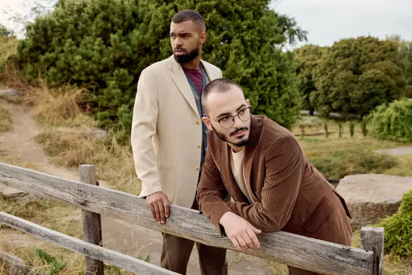 Dos hombres guapos vestidos con elegantes trajes otoñales posan en medio de la tranquila belleza de la naturaleza. - foto de stock