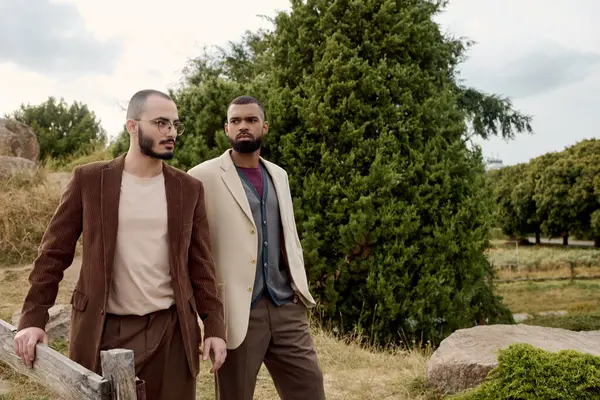 Dois homens bonitos vestindo trajes de outono na moda posar confiantemente em meio a uma paisagem pitoresca. — Fotografia de Stock