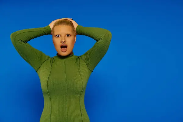 A fashionable young woman showcases her shock while posing vibrantly in front of a blue background. — Stock Photo
