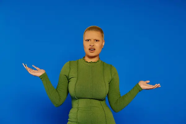 With hands raised in surprise, a young woman in a green outfit showcases bold style and emotion. — Stock Photo
